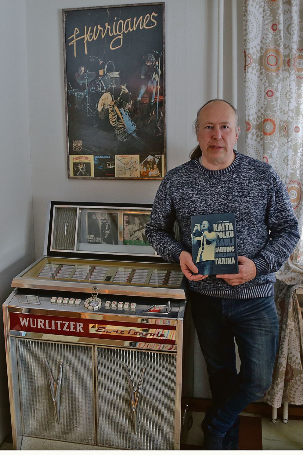 Jukka Rajala kädessään Rauli Badding Somerjoen elämänkerta Kaita polku, ja vieressään oma jukeboxi, jonka mallinen löytyy sattumoisin myös Baddingin Muotokuva 1 -LP:n kannesta.